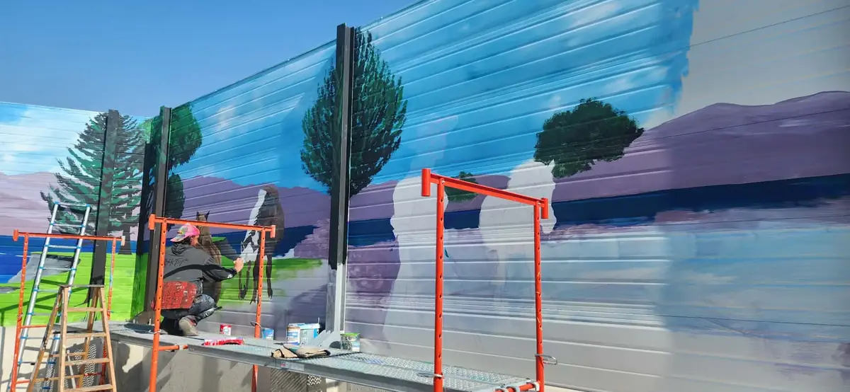 Fresque paysagère en cours sur une façade, avec l’artiste et son échafaudage
